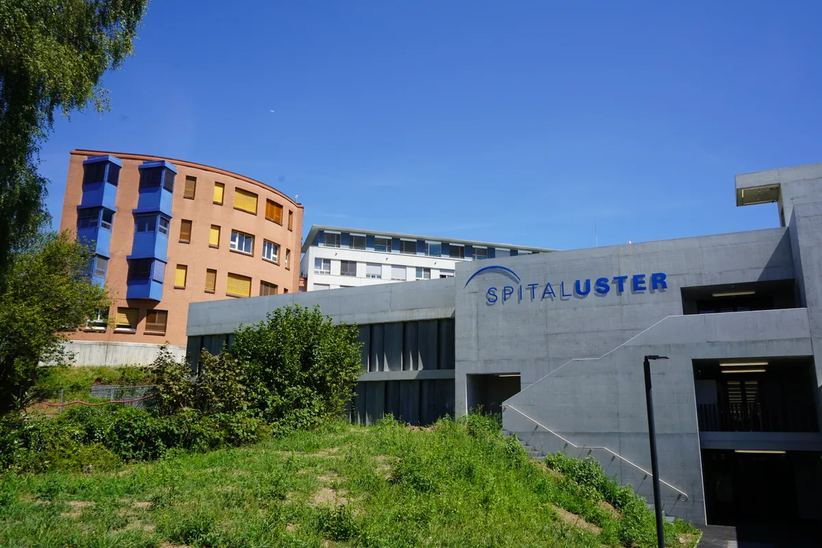 Zu sehen sind zwei verschiedenfarbige Gebäude, auf dem vorderen steht "Spital Uster"